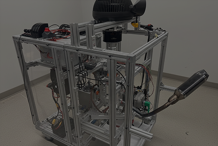 Black racing drone with four propellers and a blue motor, placed in front of a brown tactical pouch on a plain surface.