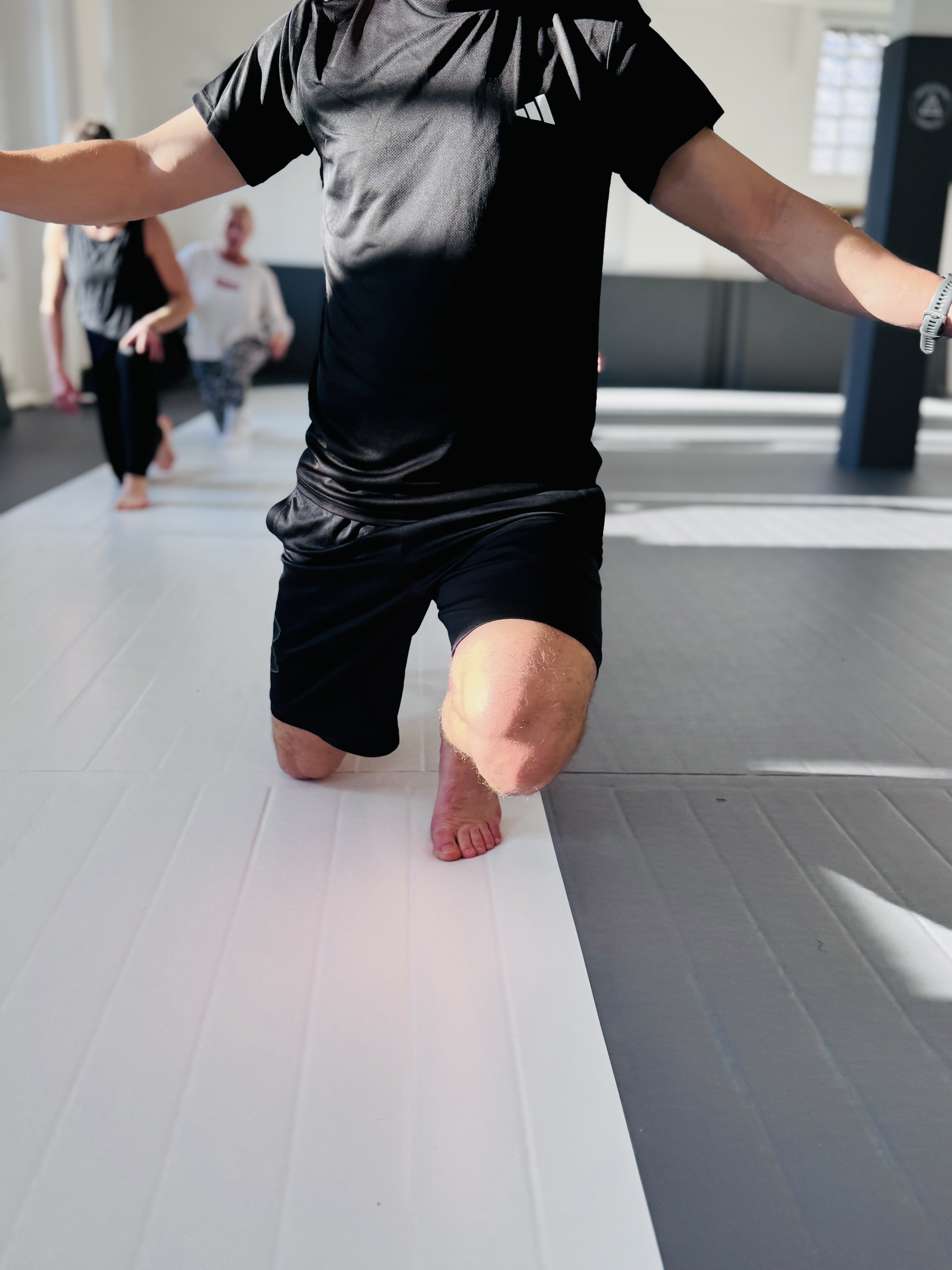 Two people practicing Brazilian jiu-jitsu on mats, wearing white gis with a training facility background.