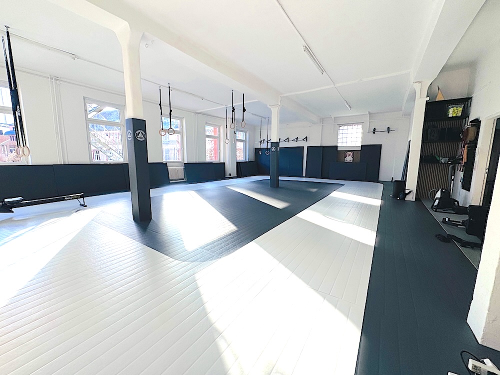 Two children practicing Brazilian Jiu-Jitsu on the floor in a bright training gym.
