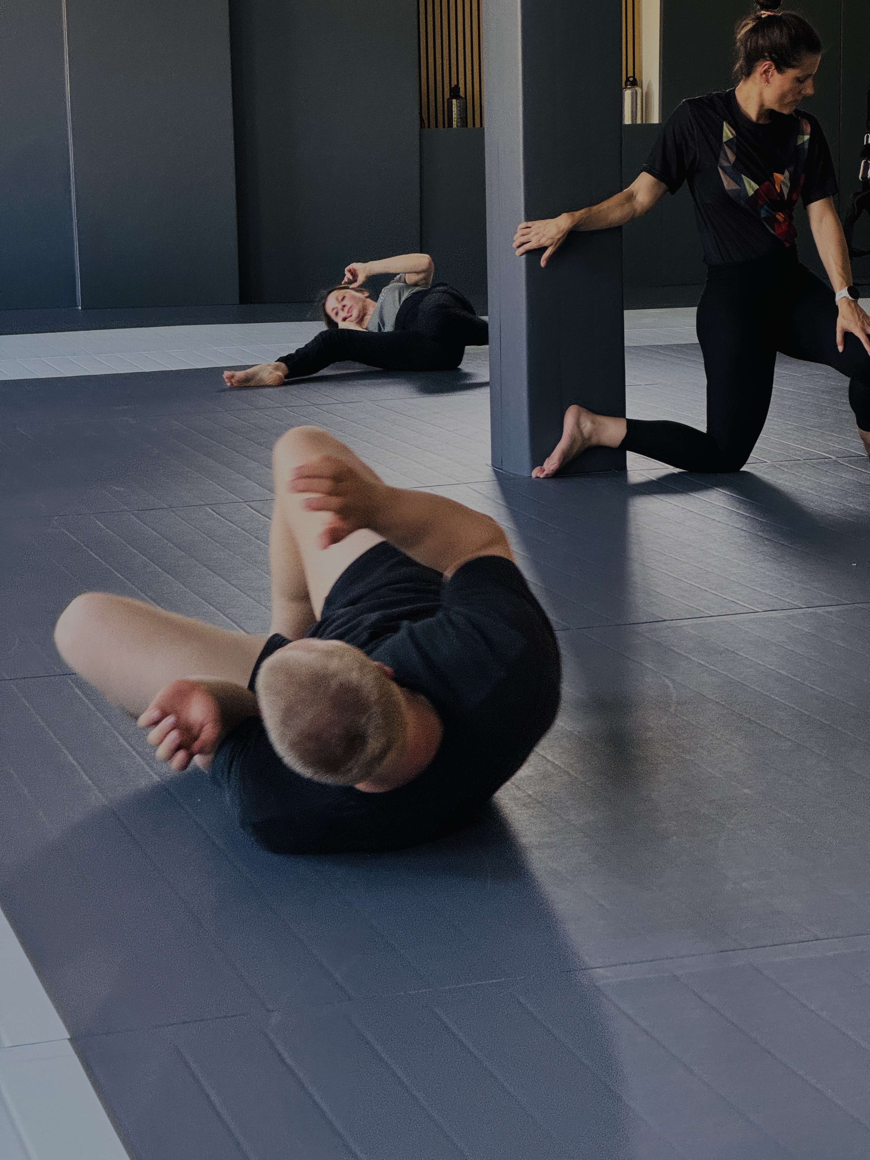 Two men wearing white martial arts gis practicing a grappling or guillotine choke technique in a bright dojo.