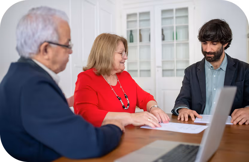 Trois personnes discutant autour d'une table avec des documents et un ordinateur portable.