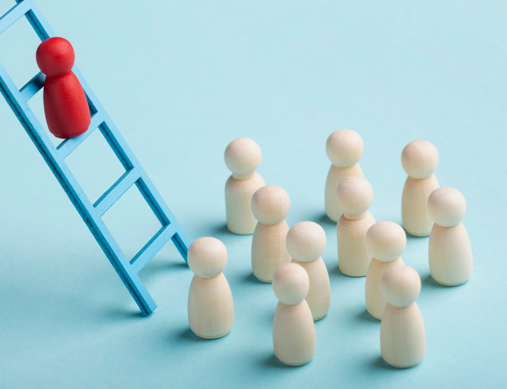 Red wooden figure climbing a blue ladder away from a group of eleven natural wood-colored figures on a light blue background.