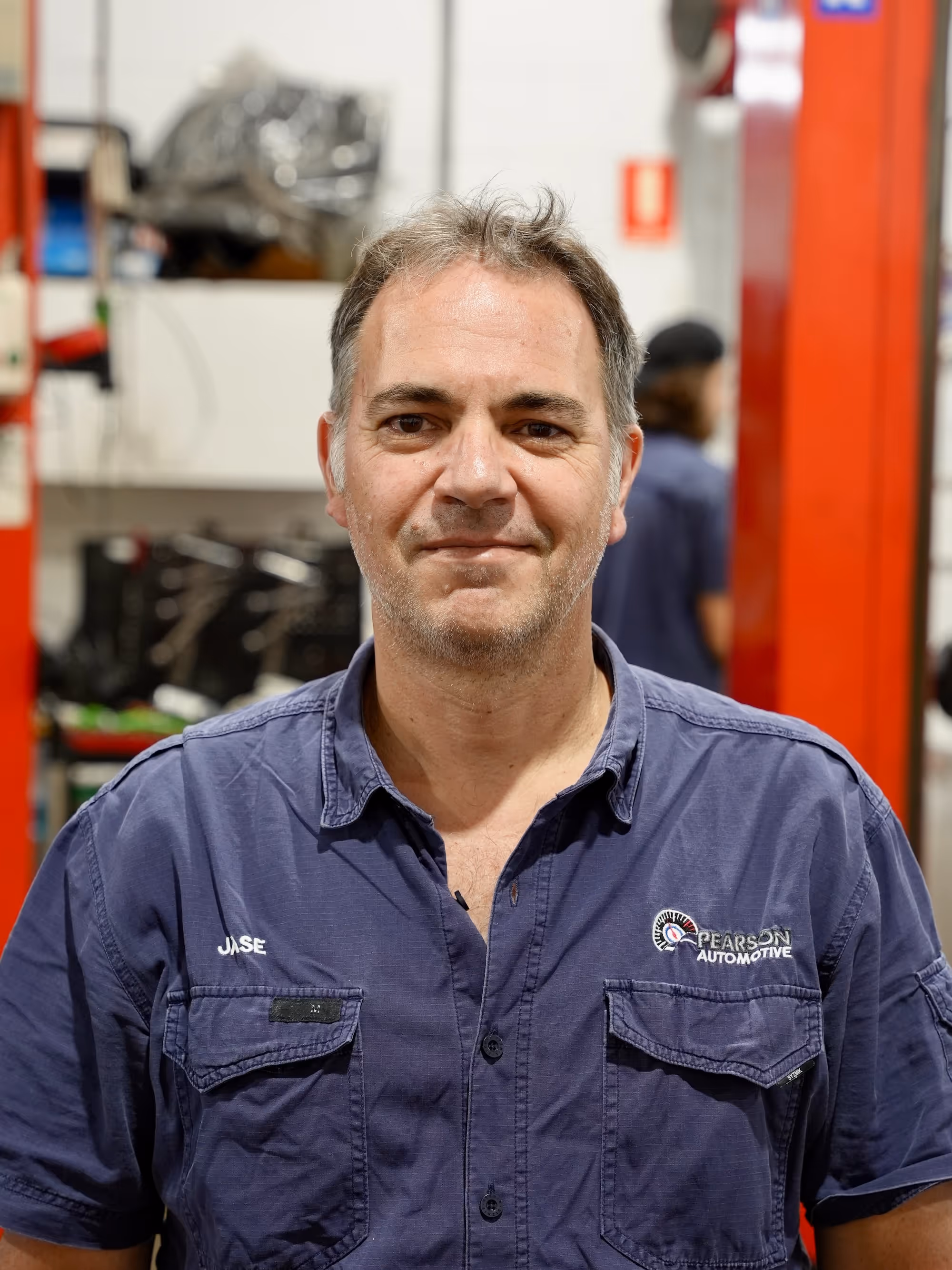 Senior automotive technician at Pearson Automotive standing confidently in front of a red tool cabinet in the Milton workshop.