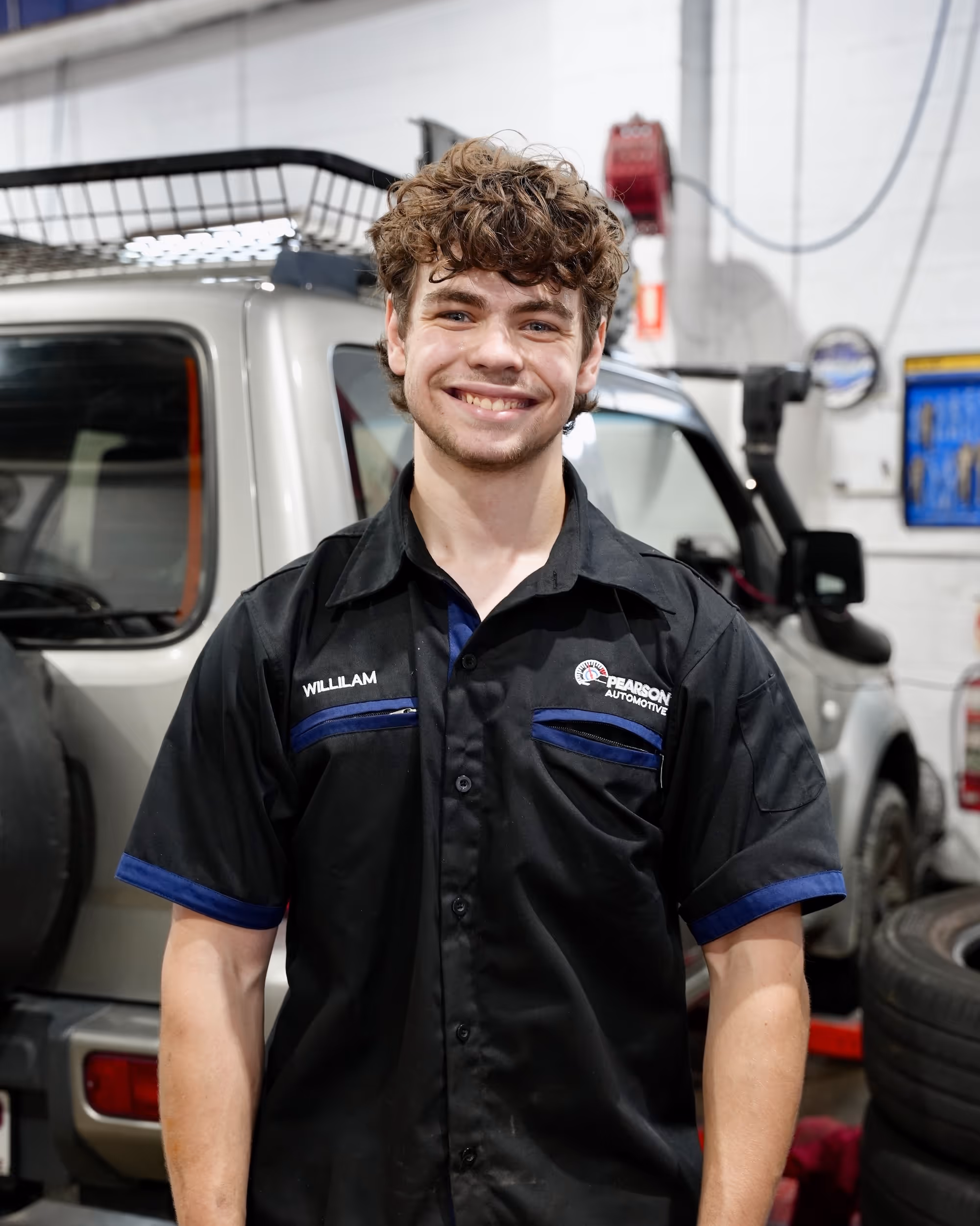 Sam, a mechanic at Pearson Automotive, wearing a blue uniform and black cap, ready to assist with car repairs.