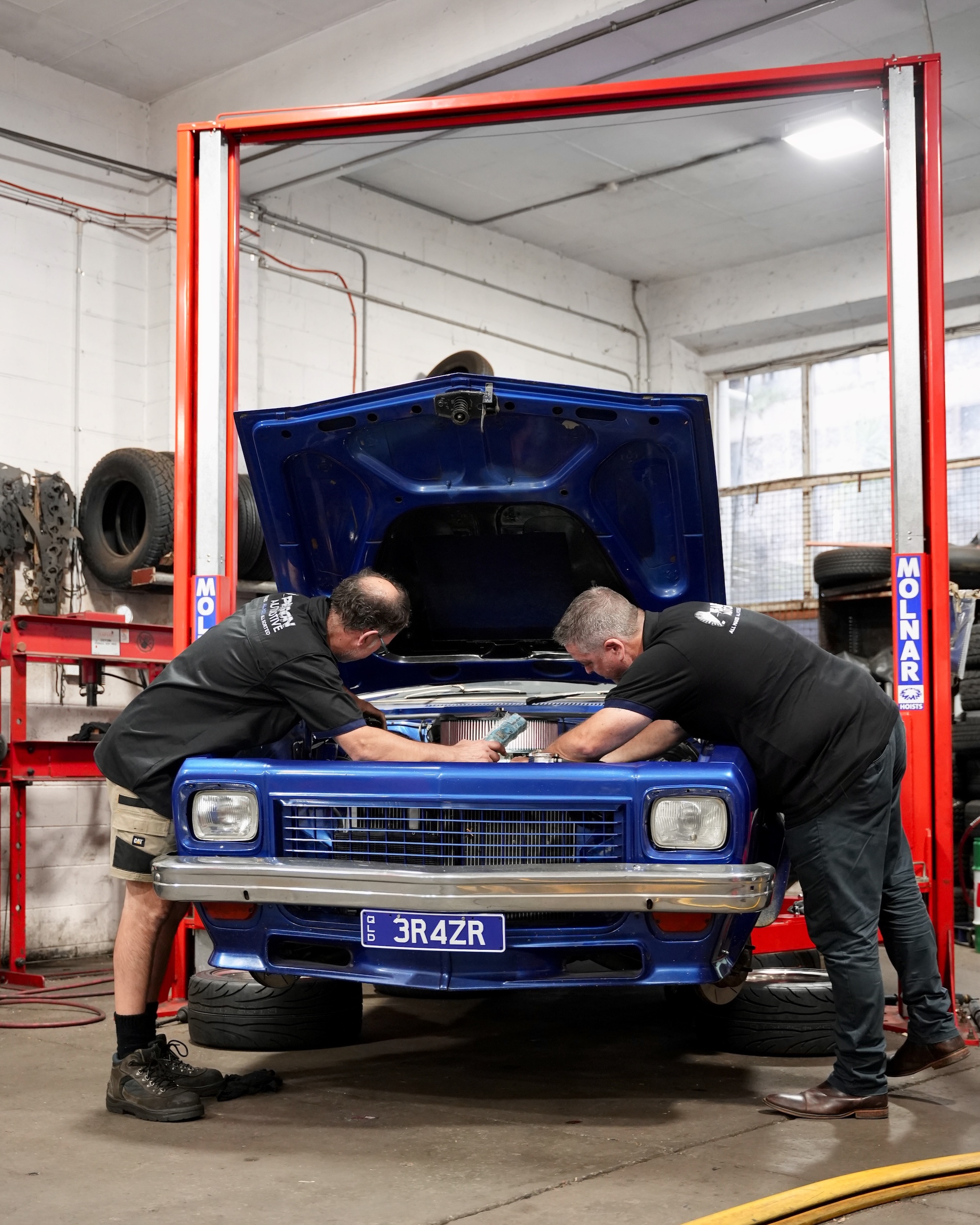 Two experienced Pearson Automotive mechanics collaborating on complex engine repairs and tuning on a vehicle in the Milton workshop.