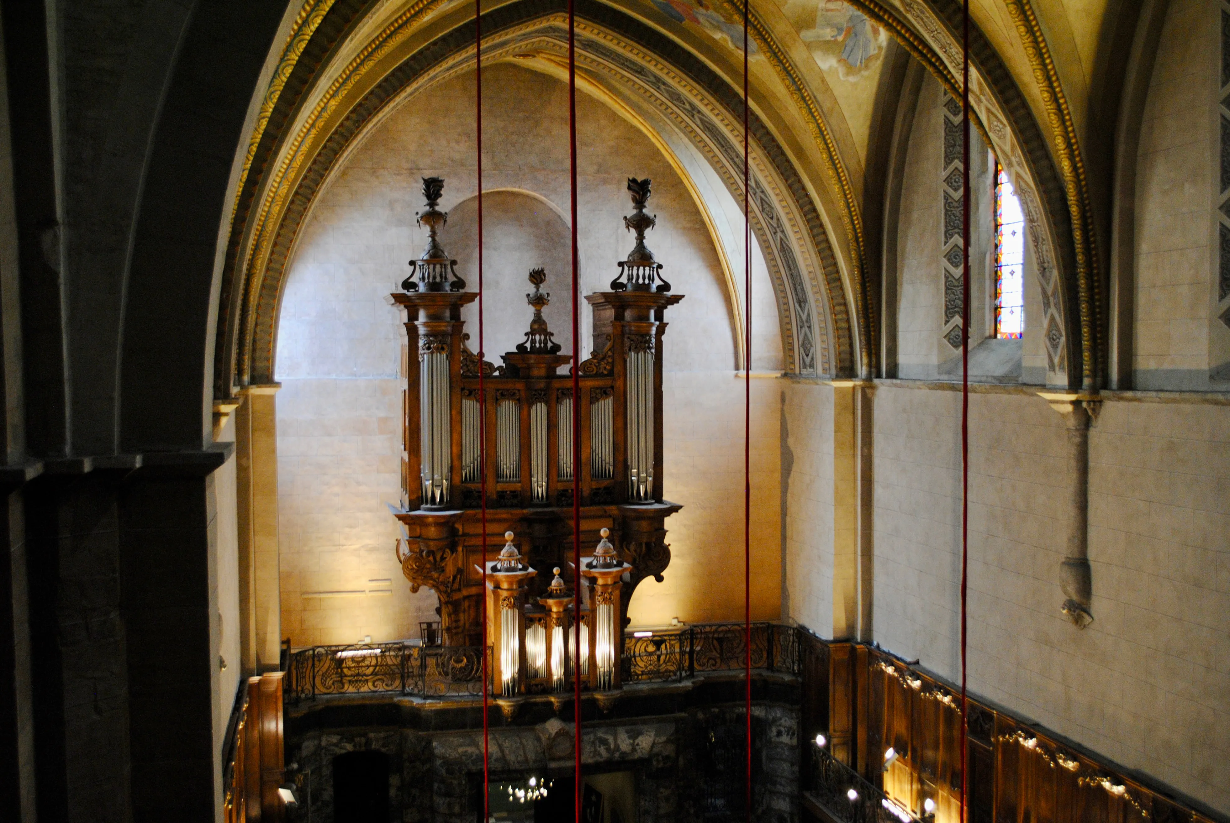 Orgue ancien en bois sculpté dans une église avec des arcs voûtés et des fenêtres colorées.