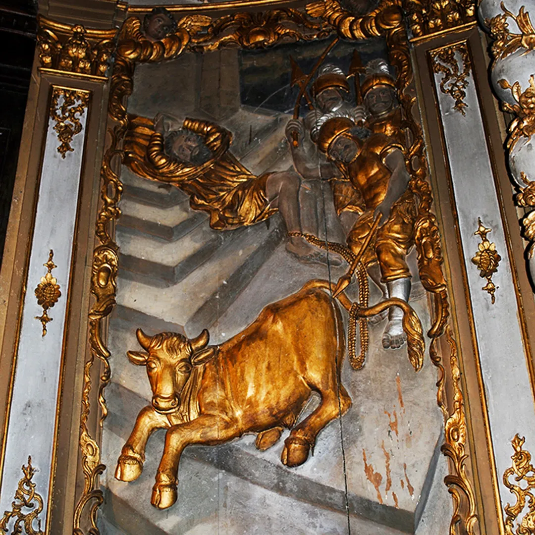Bas-relief doré représentant un taureau et trois hommes en armure sur un escalier en pierre.