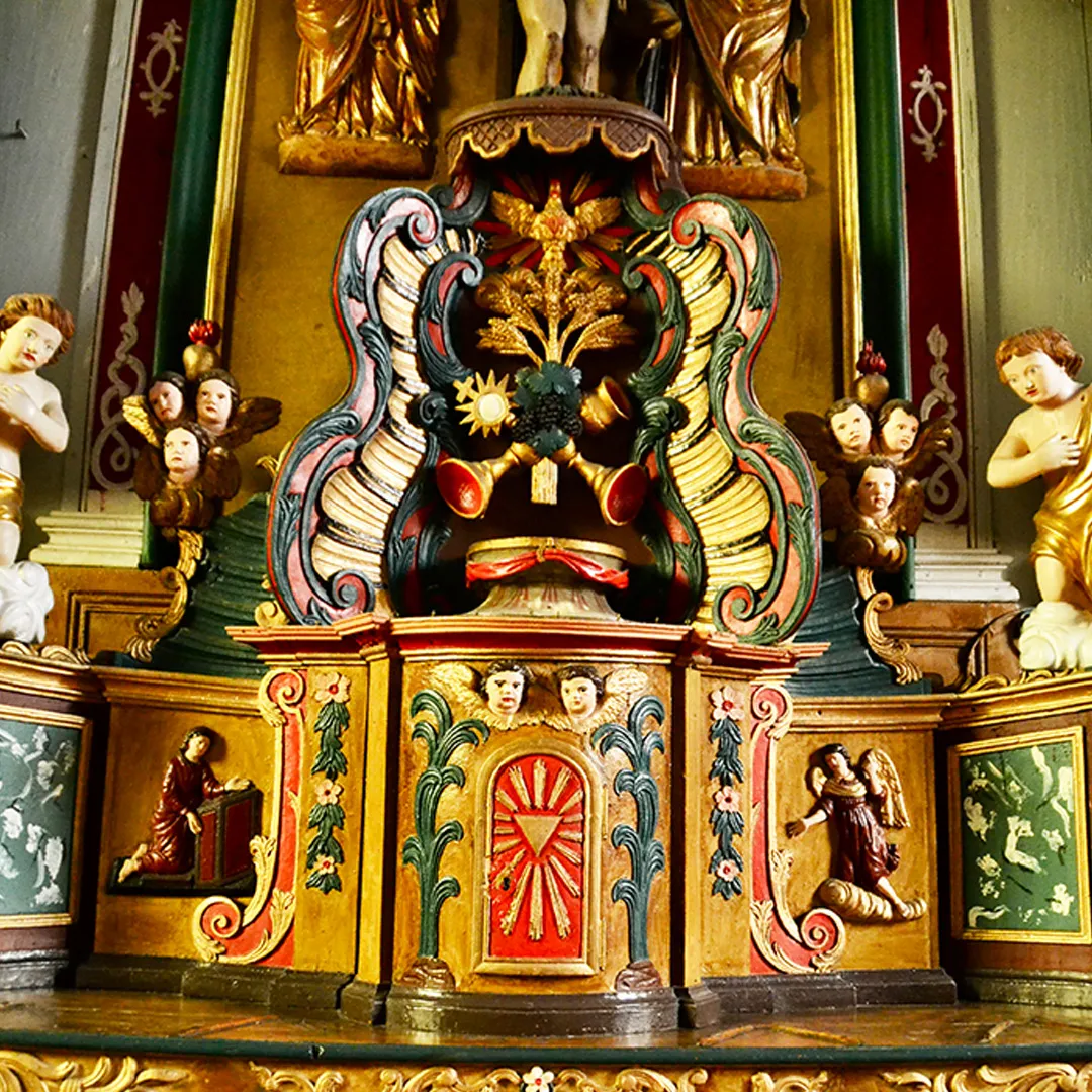 Autel d'église orné de sculptures colorées d'anges, d'instruments et de motifs floraux.