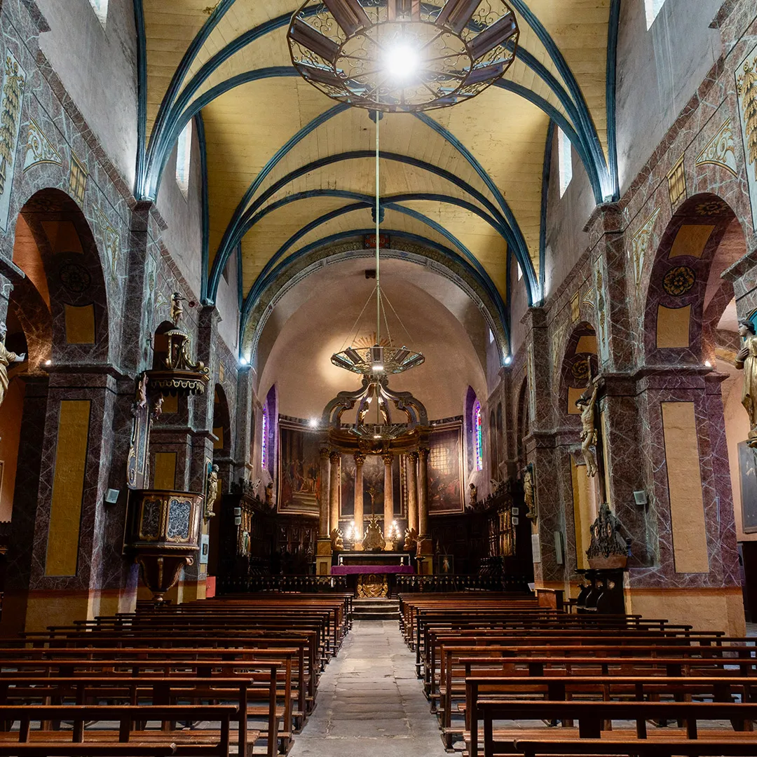 Nef d'église avec des bancs en bois, arches décorées et un autel éclairé au fond.
