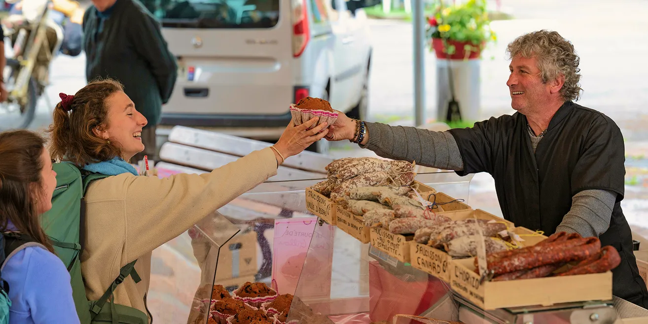 Une cliente souriante reçoit un muffin d'un vendeur de charcuterie à un marché en plein air.