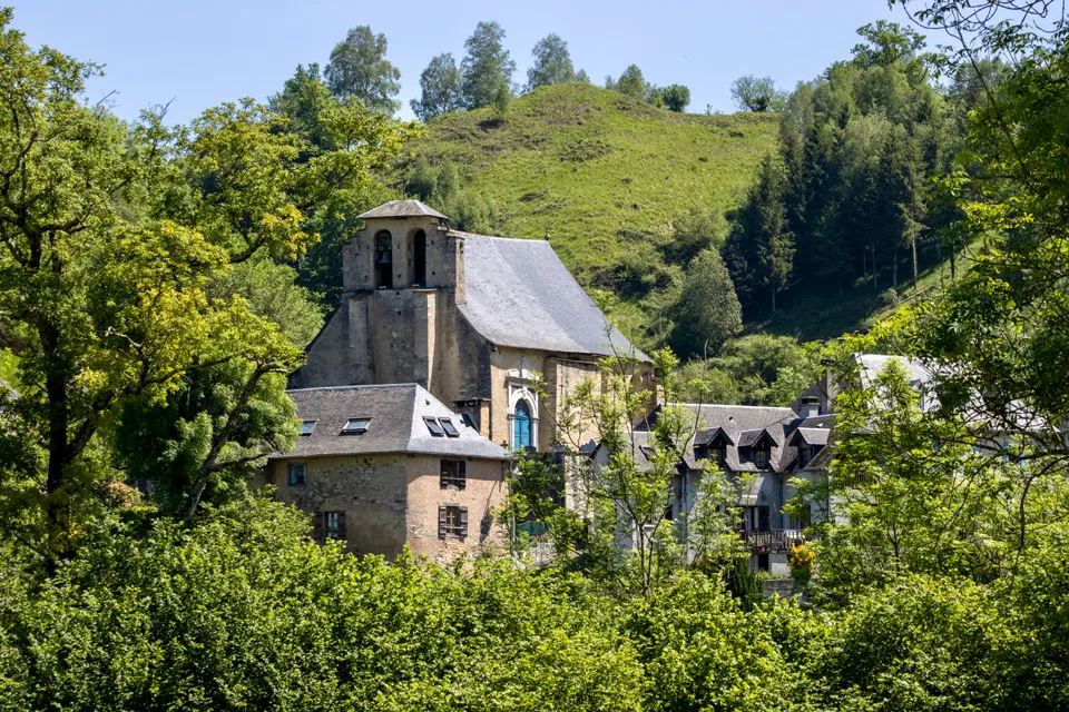 Village avec des maisons en pierre et une église entourées d'arbres et de collines verdoyantes.