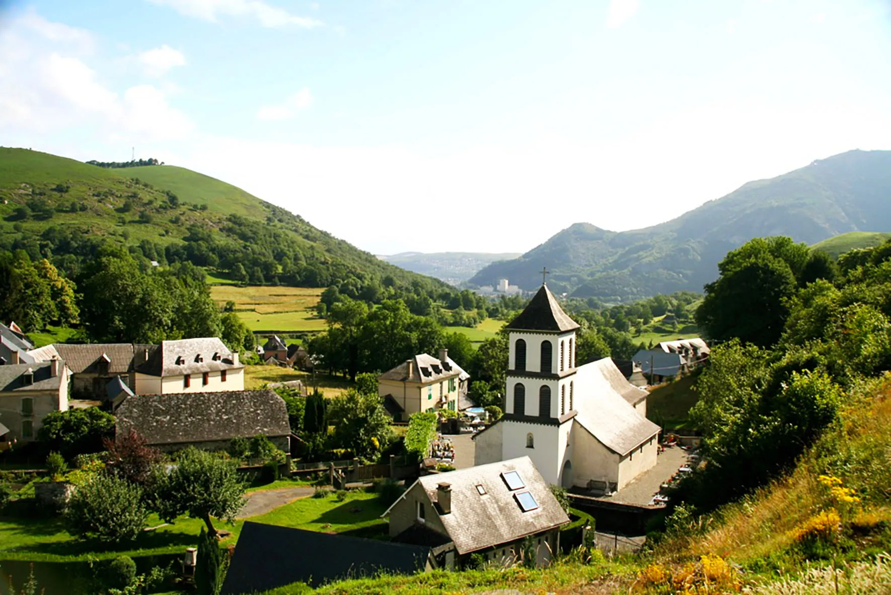 Village pittoresque avec une église au clocher blanc au centre entourée de collines verdoyantes.