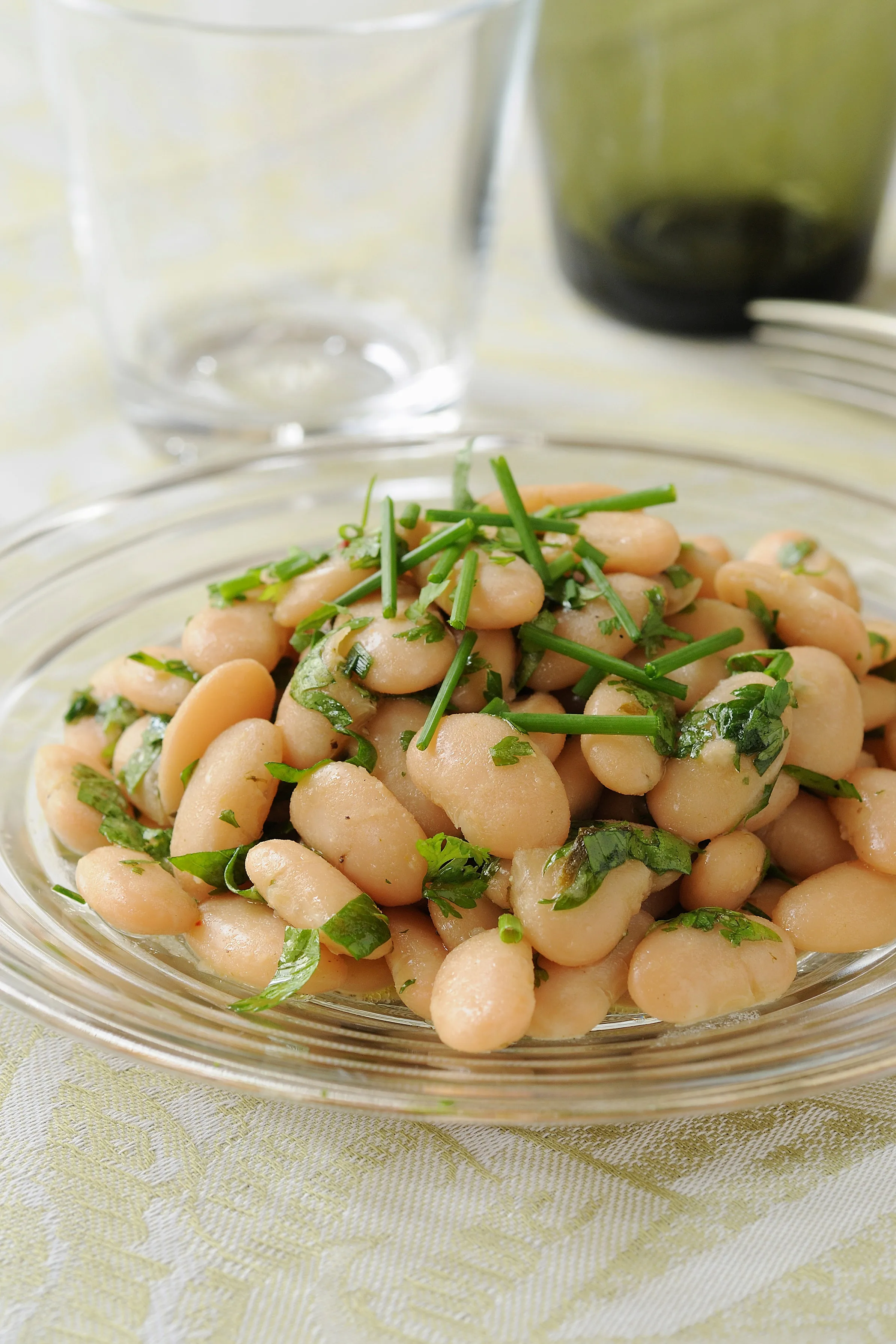 Haricots blancs cuits assaisonnés d'herbes fraîches dans une assiette en verre.