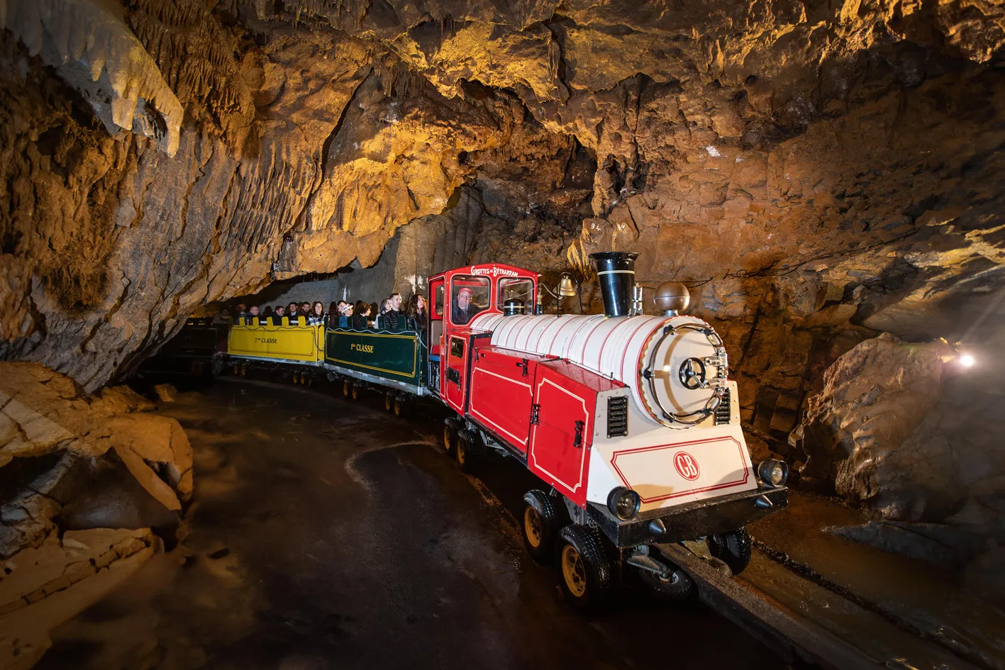 Petit train rouge avec des passagers circulant dans une grotte aux parois rocheuses éclairées.