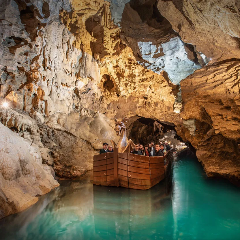 Un groupe de personnes en bateau sur une eau turquoise dans une grotte aux formations rocheuses éclairées.
