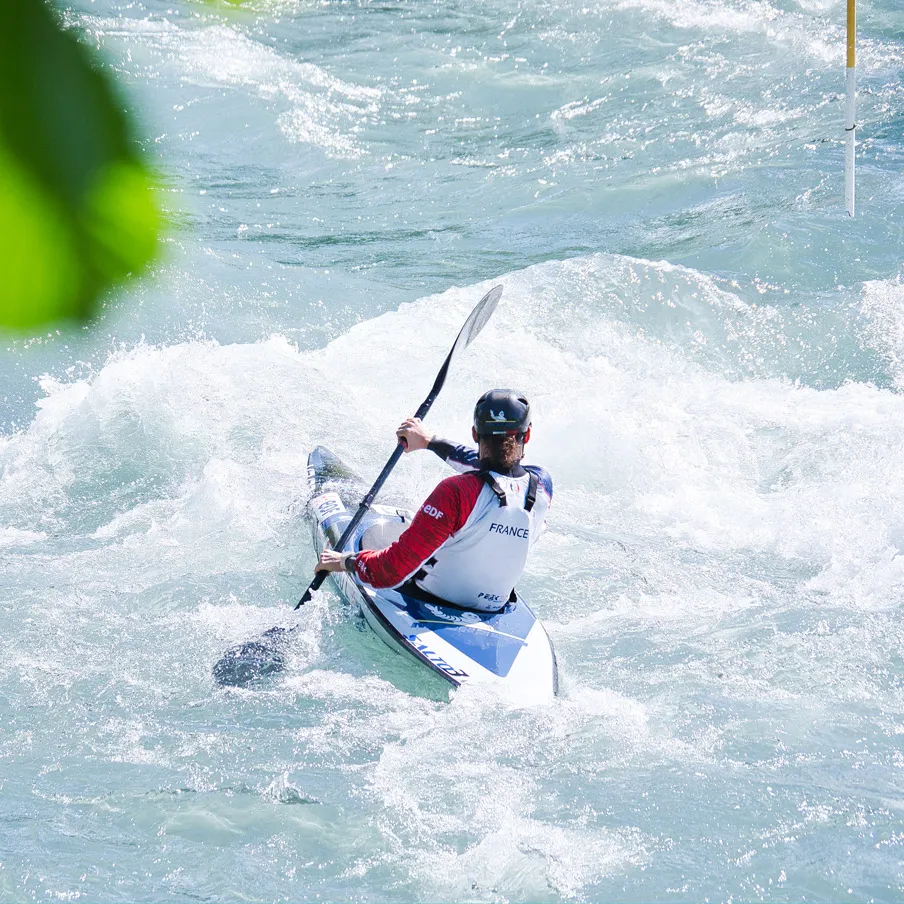Canoéiste français en kayak slalom pagayant dans l'eau agitée d'une rivière.