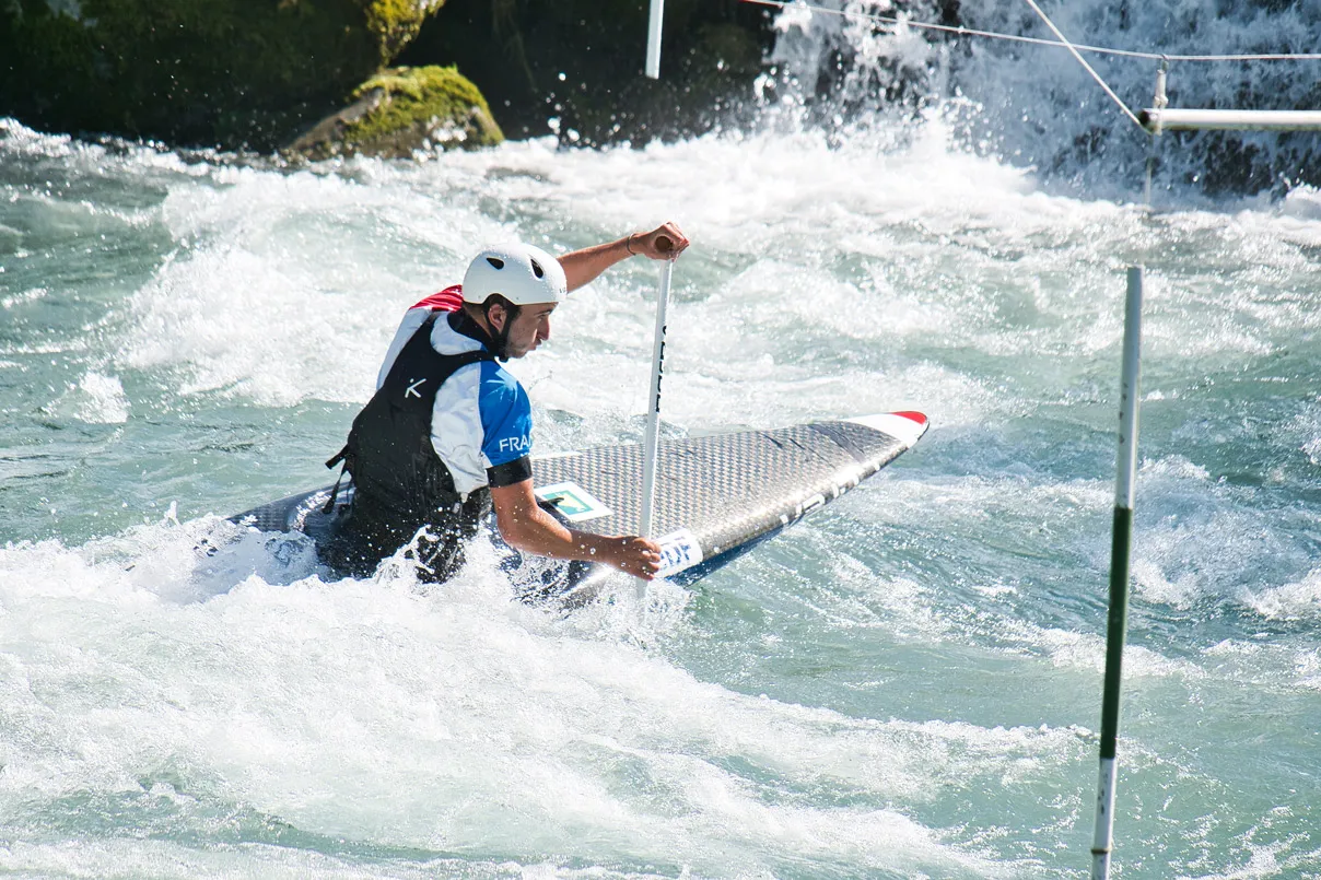 Canoéiste portant un casque naviguant dans des rapides sous les portes d'un parcours de slalom.