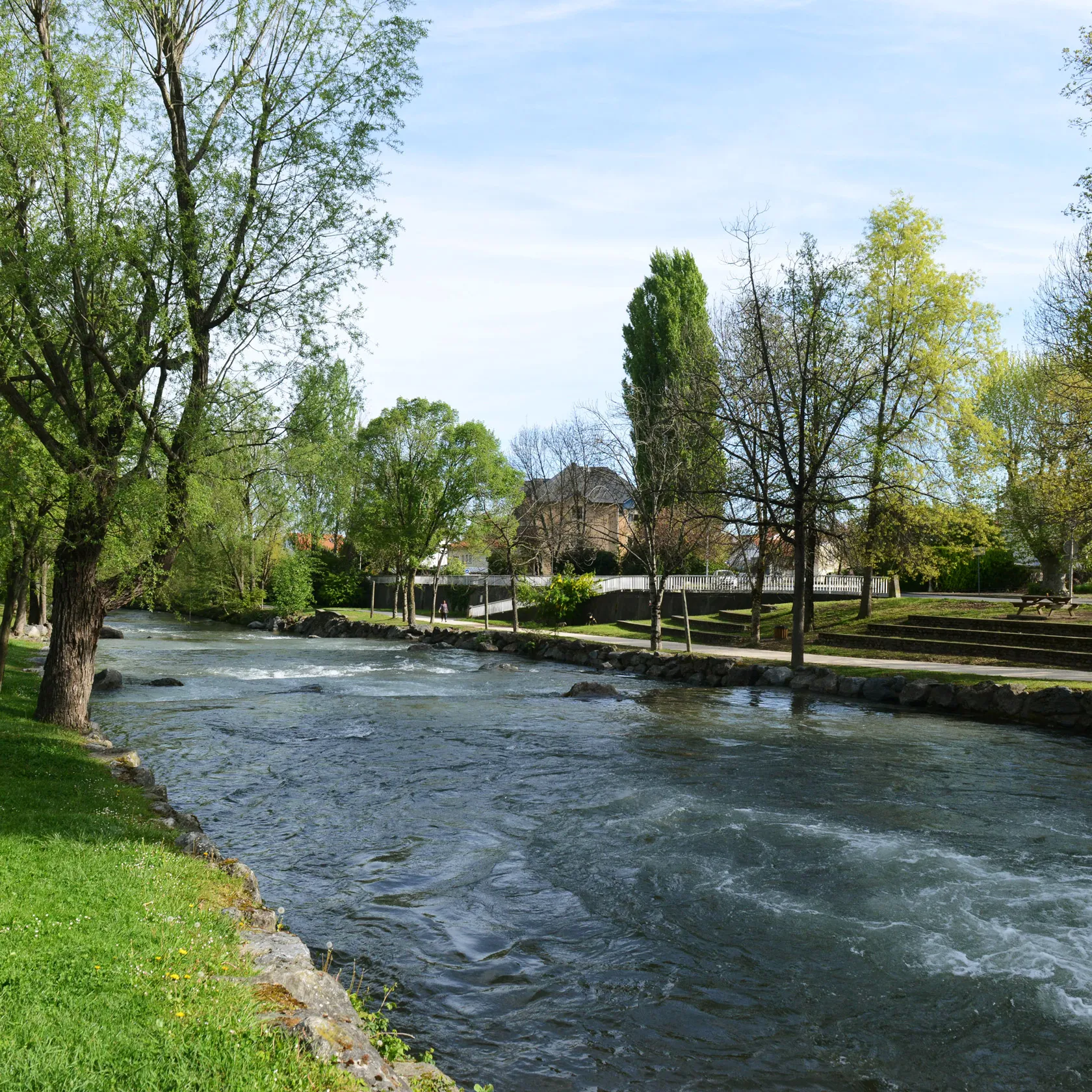 Rivière large avec eaux agitées bordée d'arbres et d'un parc avec pelouse verte claire.