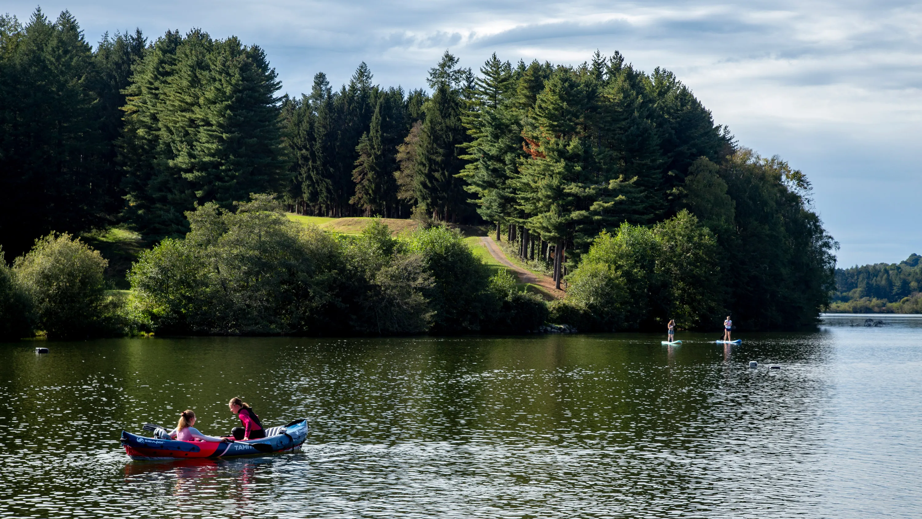 Deux personnes en kayak sur un lac entouré de forêt et deux autres sur des paddle boards.