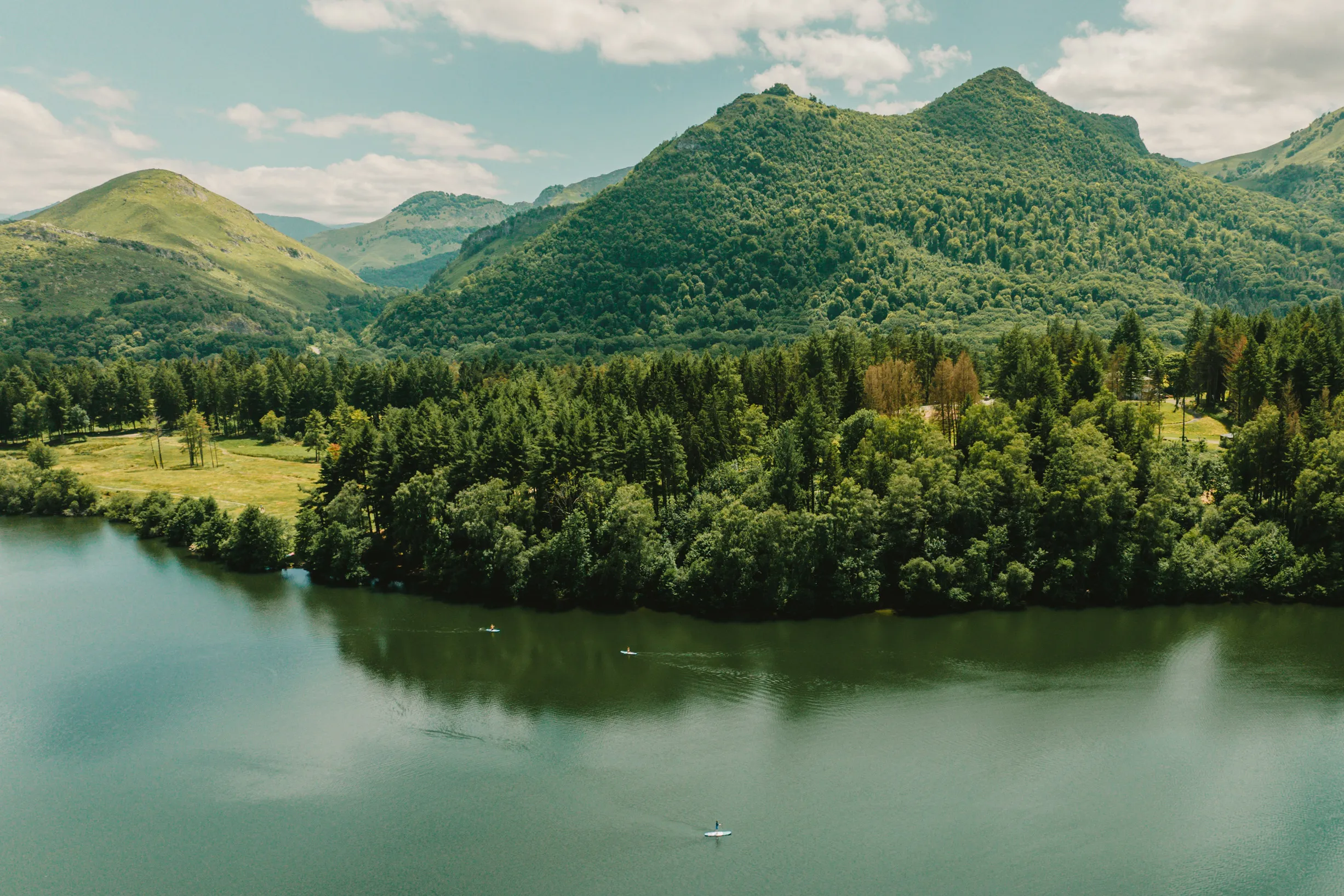 Trois personnes pagayant sur un lac calme entouré de collines et de forêts verdoyantes.