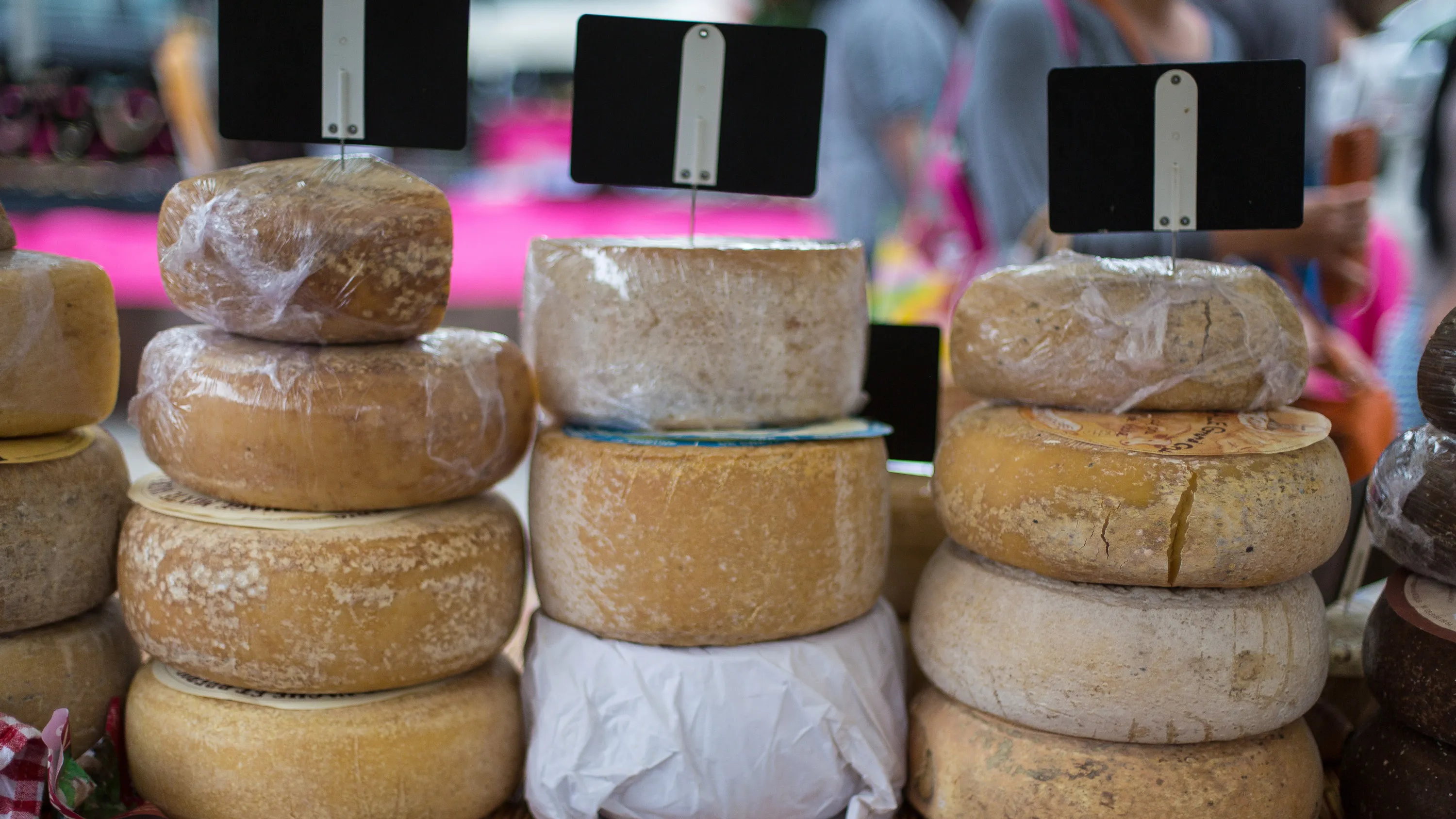 Piles de fromages ronds variés emballés avec des étiquettes noires sur un marché.