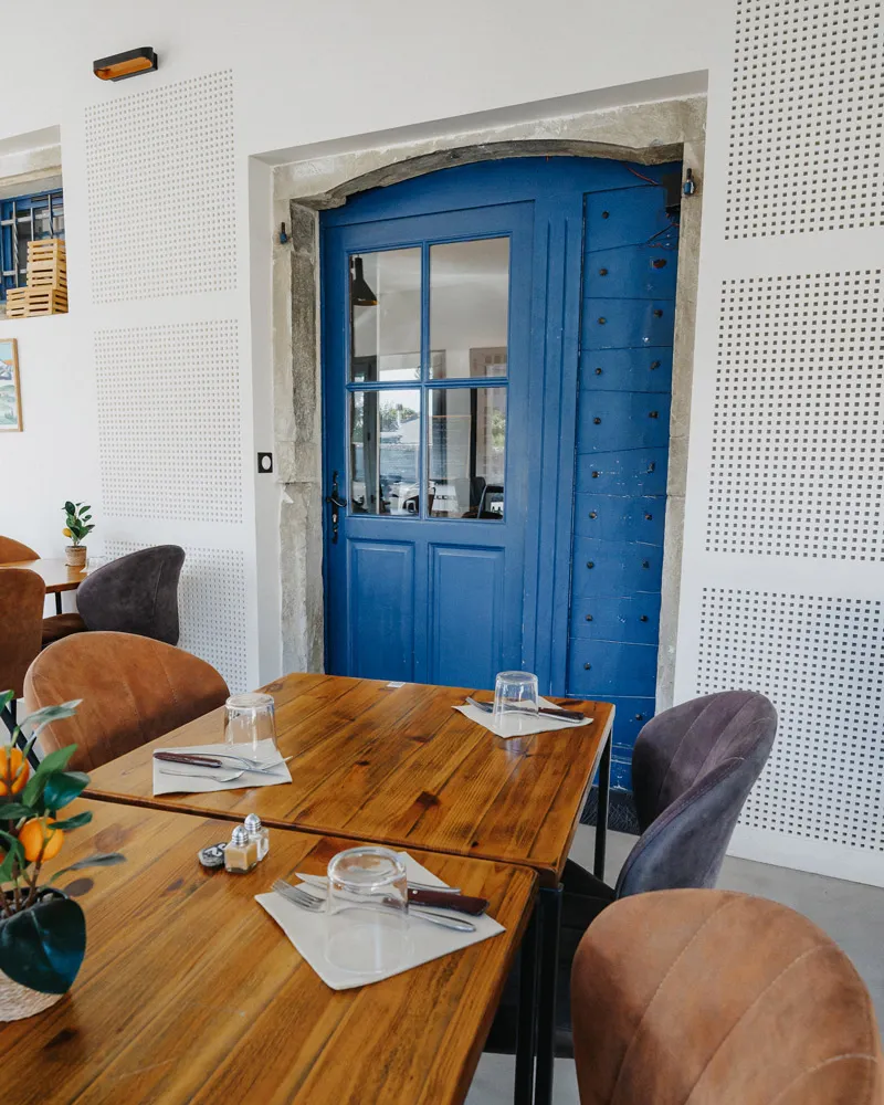 Table en bois dressée avec couverts et verres devant une porte bleue dans un restaurant moderne.