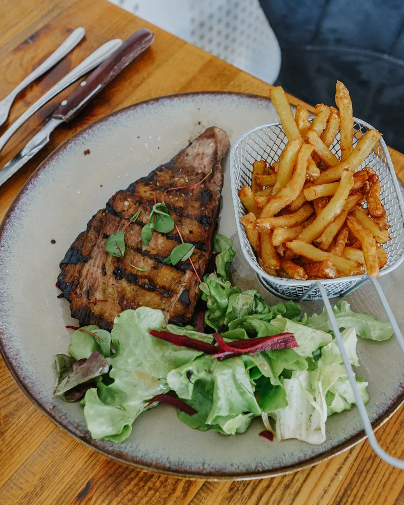 Grillade de viande avec salade verte et frites dans un petit panier métallique sur une assiette.