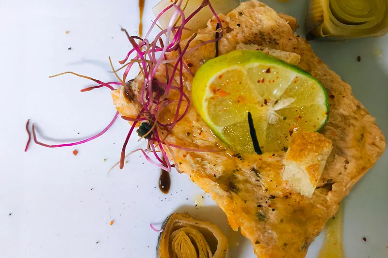 Plat gourmet avec rillette de truite, tranche de citron, pousses violettes et artichauts en garniture.