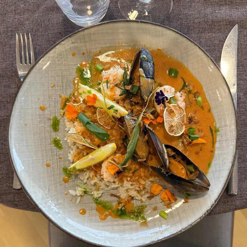 Assiette de riz avec moules, crevettes, sauce orange, herbes, tranches de citron et fleurs comestibles.