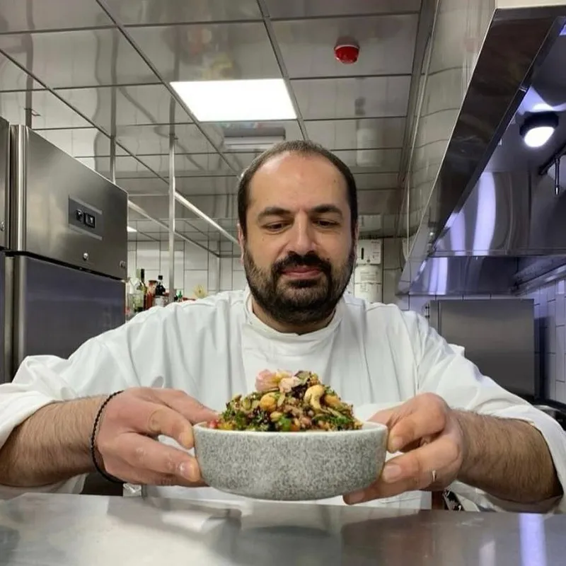 Chef dans une cuisine professionnelle tenant un bol contenant un plat coloré aux noix et légumes.