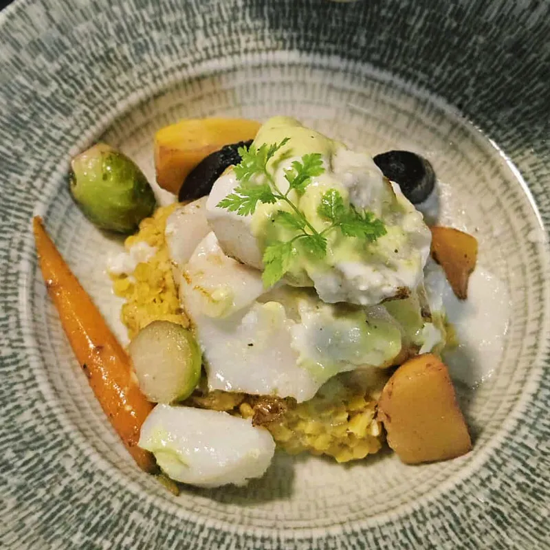 Assiette de poisson blanc avec sauce verte, légumes variés et purée jaune.