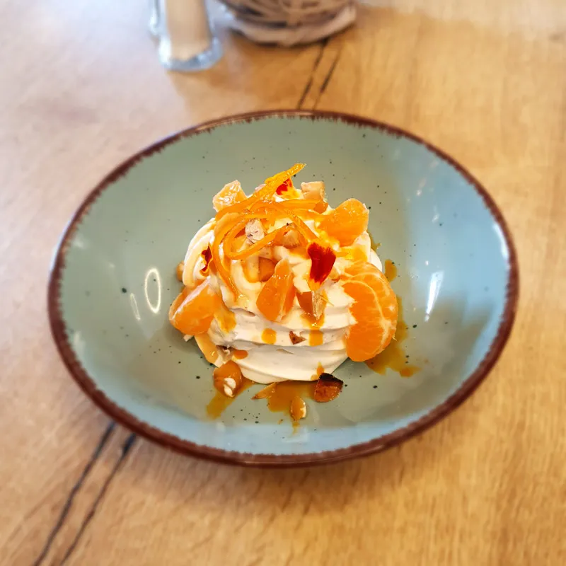 Dessert crémeux avec quartiers de mandarine, zestes et éclats de noix dans un bol bleu.