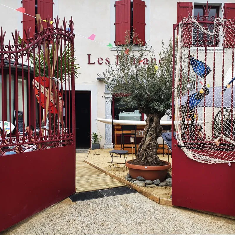 Entrée avec portail rouge ouvrant sur terrasse avec arbre en pot et décoration marine.