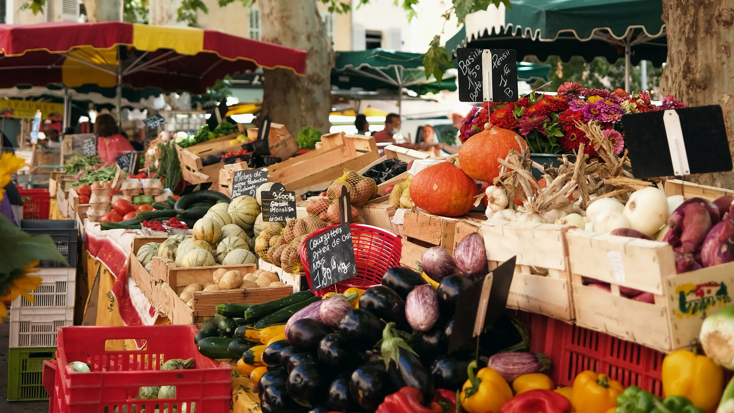Étalage de légumes frais et fleurs sous des tentures colorées à un marché en plein air.