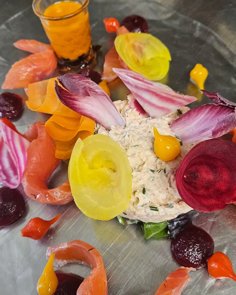 Assiette gourmande avec mousse, légumes colorés, tranches de saumon et petites sauces orange et rouges.