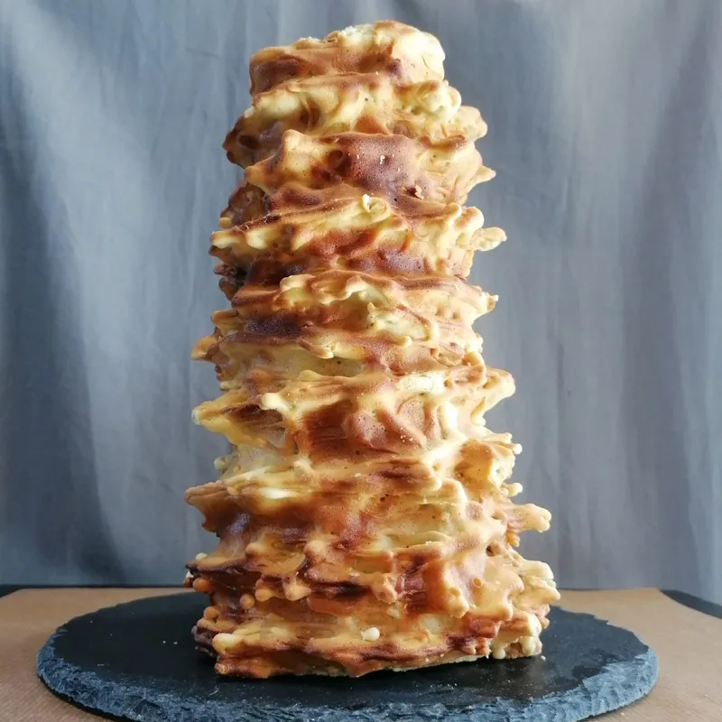 Un gâteau à la broche doré et irrégulier posé sur un plateau noir rond.