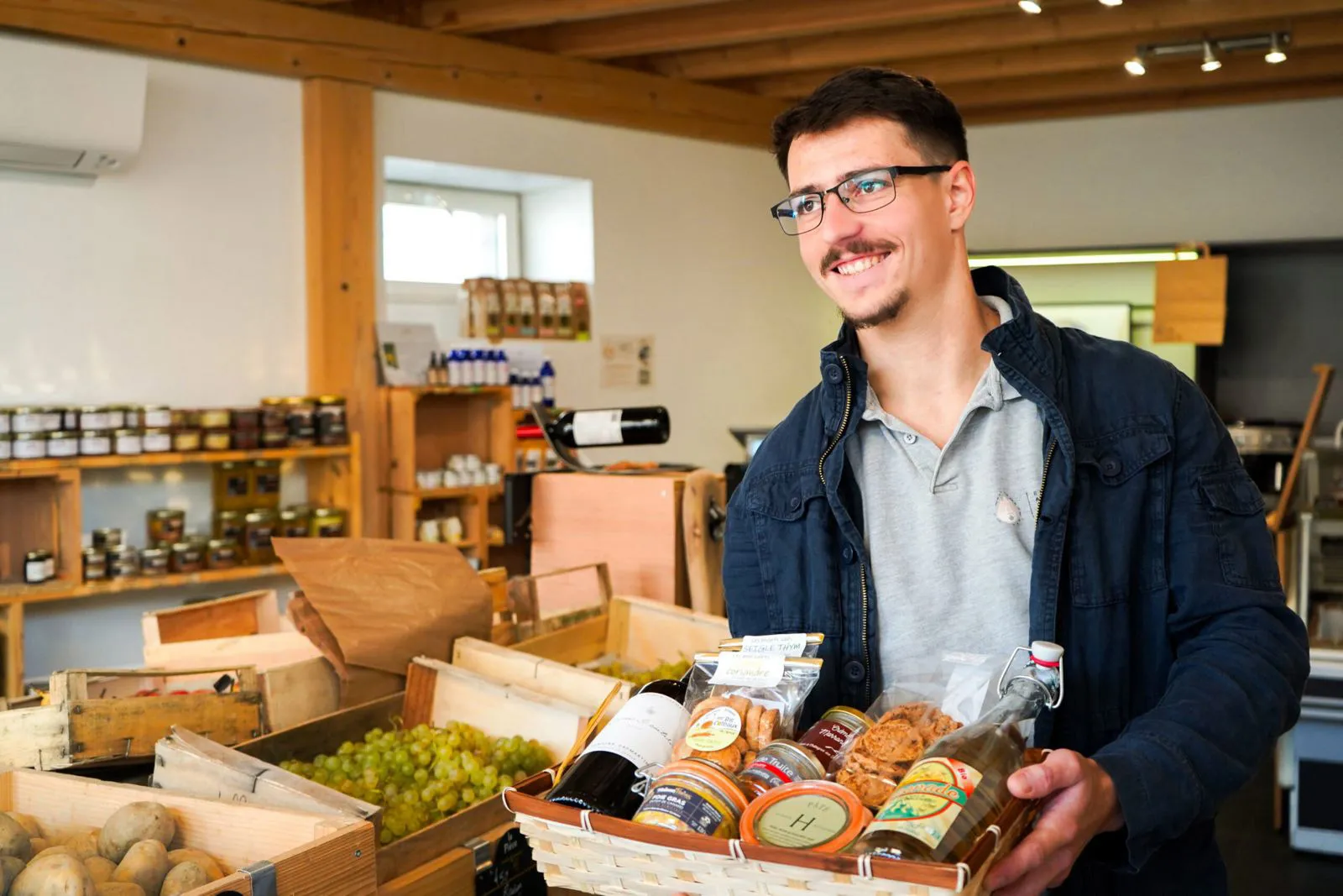 Homme souriant portant un panier rempli de produits alimentaires dans un magasin fermier.