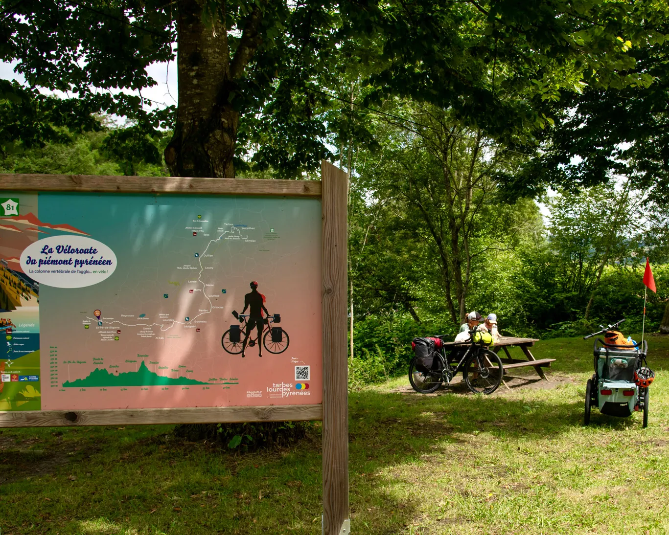 Carte de La Véloroute du piémont pyrénéen en bois, avec deux cyclistes assis à une table en bois.