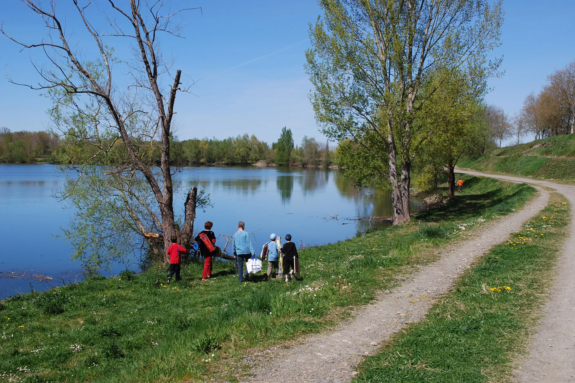 Un groupe de personnes marchant près d'un lac entouré d'arbres sous un ciel bleu clair.