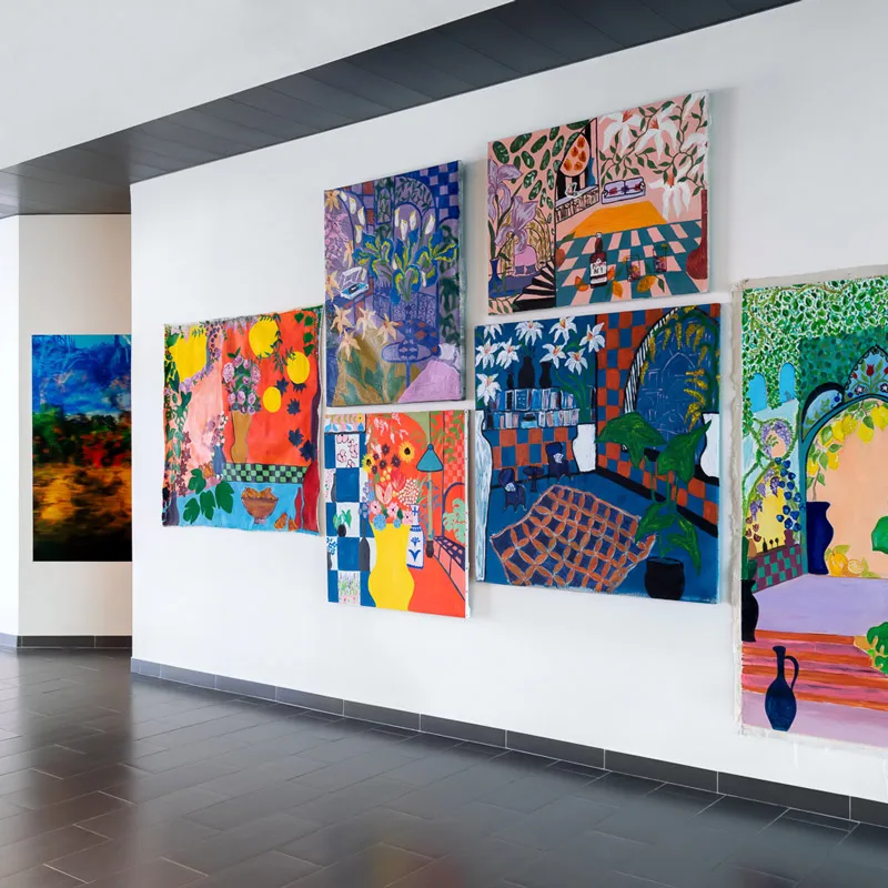Galerie d'art avec sept toiles colorées suspendues sur un mur blanc moderne.