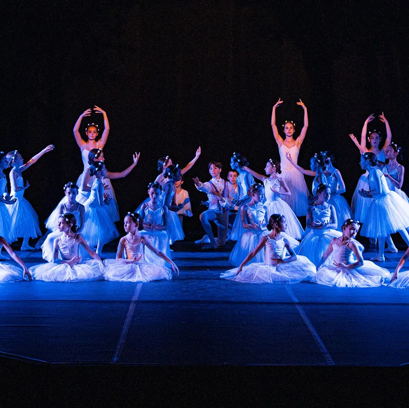 Danseuses en tutus blancs exécutant une chorégraphie sur scène éclairée en bleu.