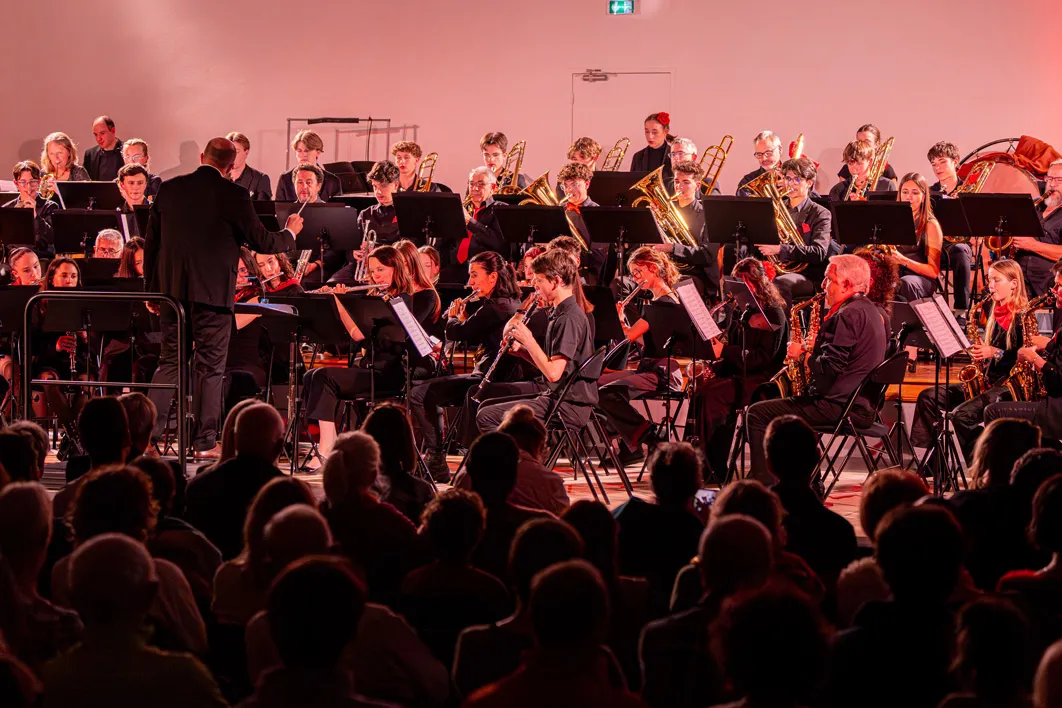 Orchestre symphonique lors d'un concert, dirigé par un chef devant un public nombreux.