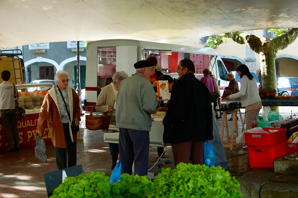 Marché de plein air sous un abri avec des stands et des clients achetant des produits frais.