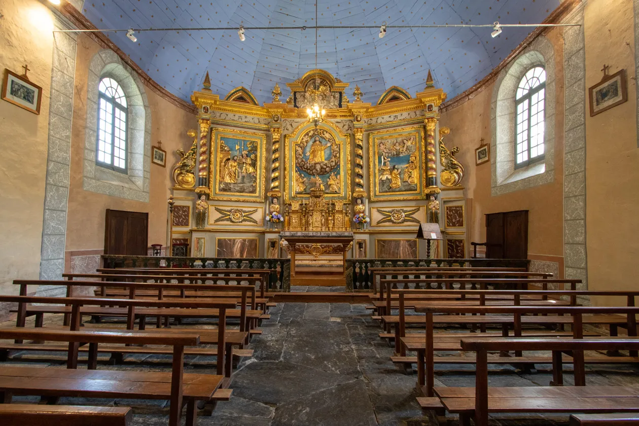 Intérieur d'une chapelle avec un autel baroque doré et des bancs en bois alignés sur un sol de pierre.