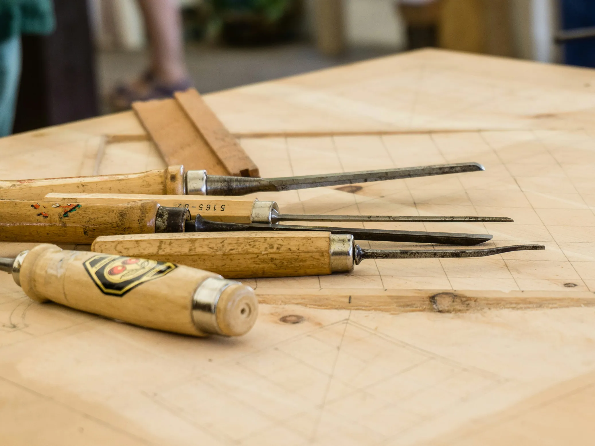 Outils de sculpture sur bois avec manches en bois posés sur une surface en bois clair marquée.