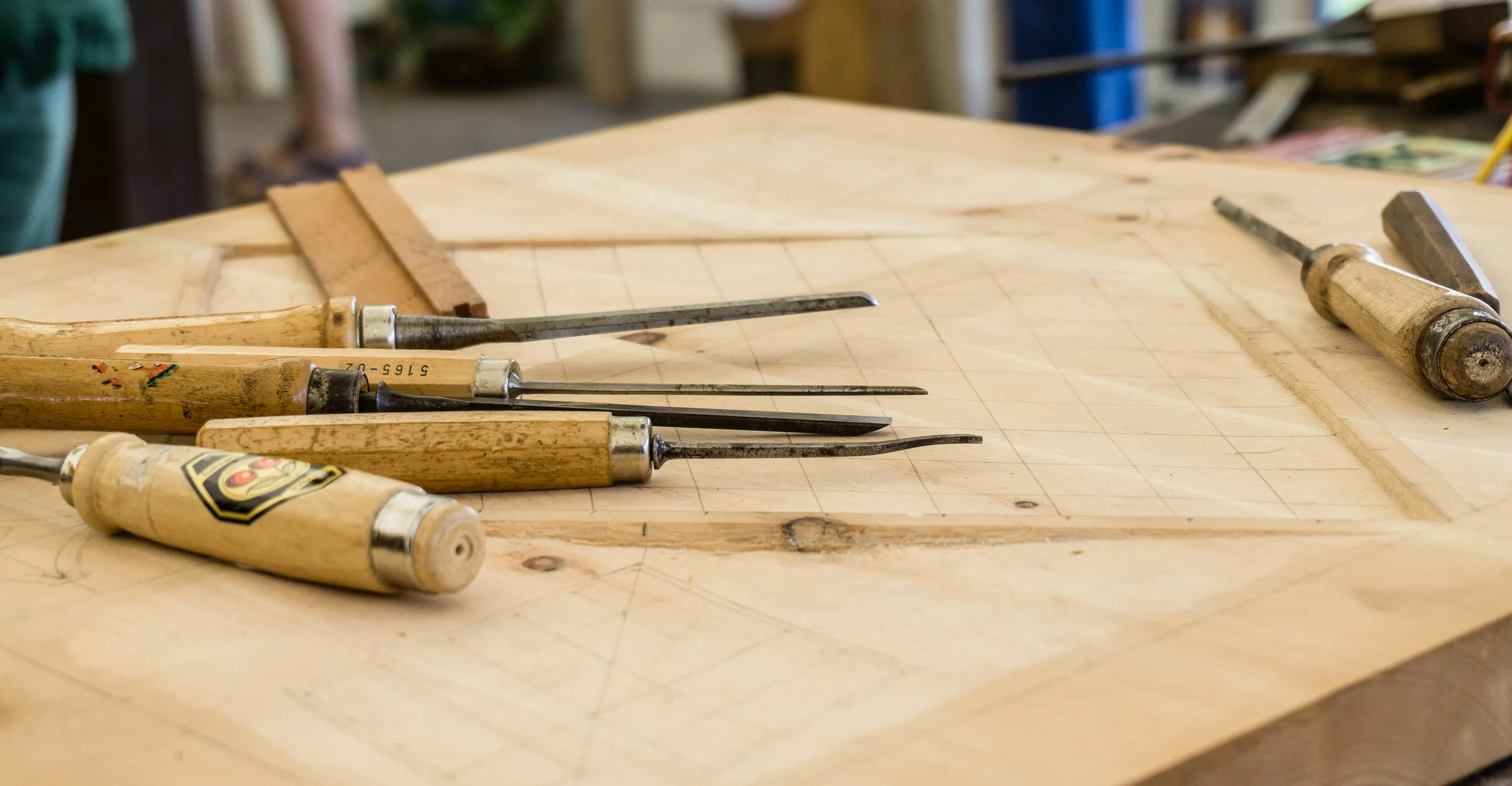 Outils de sculpture sur bois en bois et métal posés sur une planche de bois marquée de lignes.