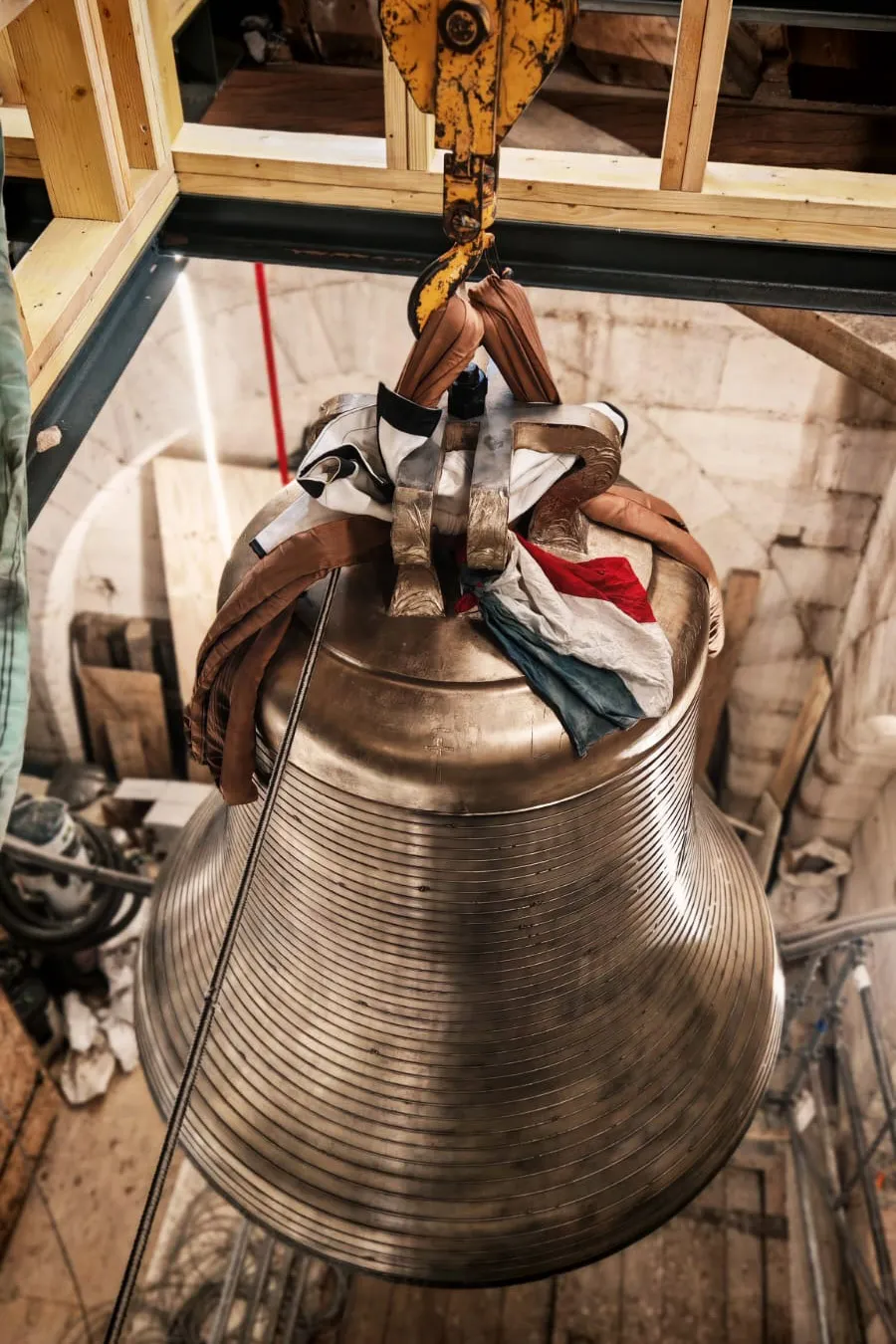 Cloche suspendue par une grue dans une tour en pierre avec un drapeau français drapé dessus.