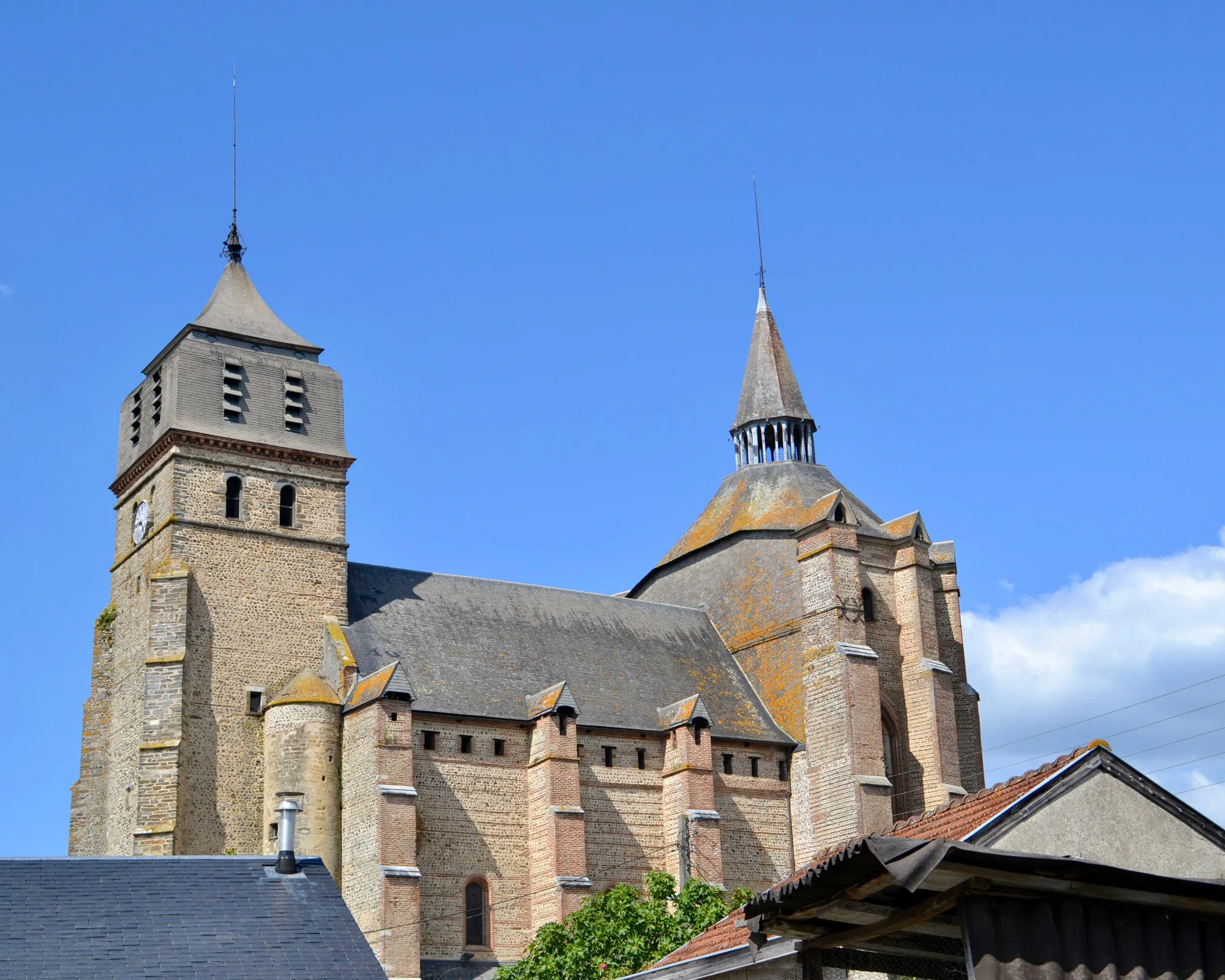 Église ancienne en pierre avec une tour horloge et un clocher sous un ciel bleu clair.