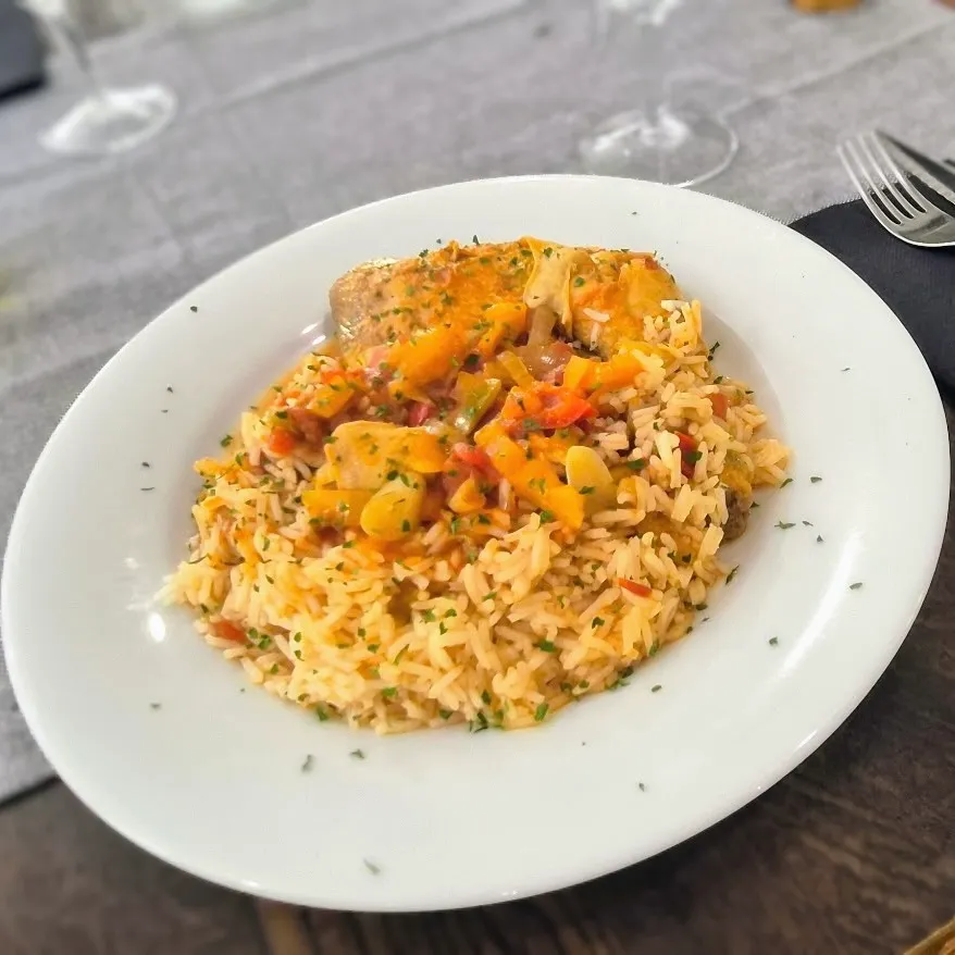 Assiette de riz aux légumes colorés et morceaux de viande, garnie d'herbes fraîches.