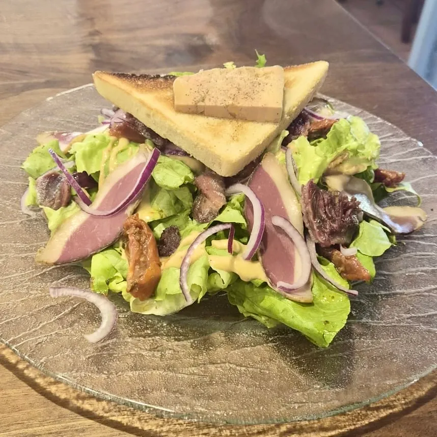 Salade avec laitue, oignons rouges, tranches de viande, toast triangulaire et sauce.